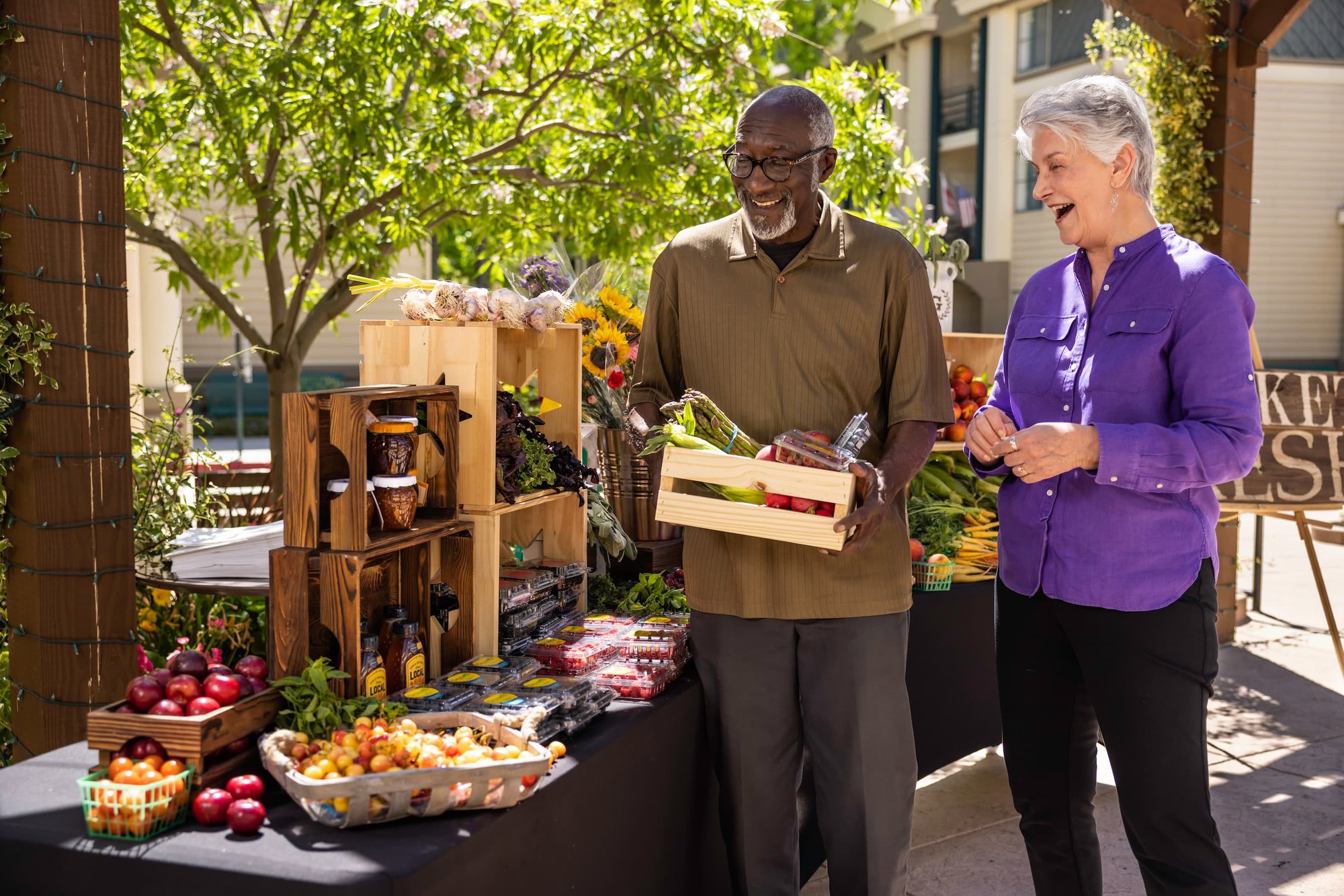 Two smiling residents browse produce at a farmer’s market stall. 