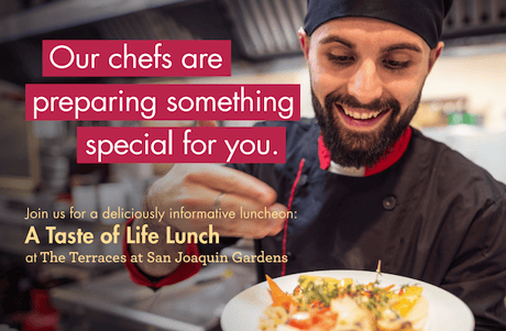 Chef smiling and holding a colorful plated dish.