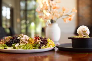 A plated salad and a dessert with ice cream in an elegant dining setting with flowers in the background.