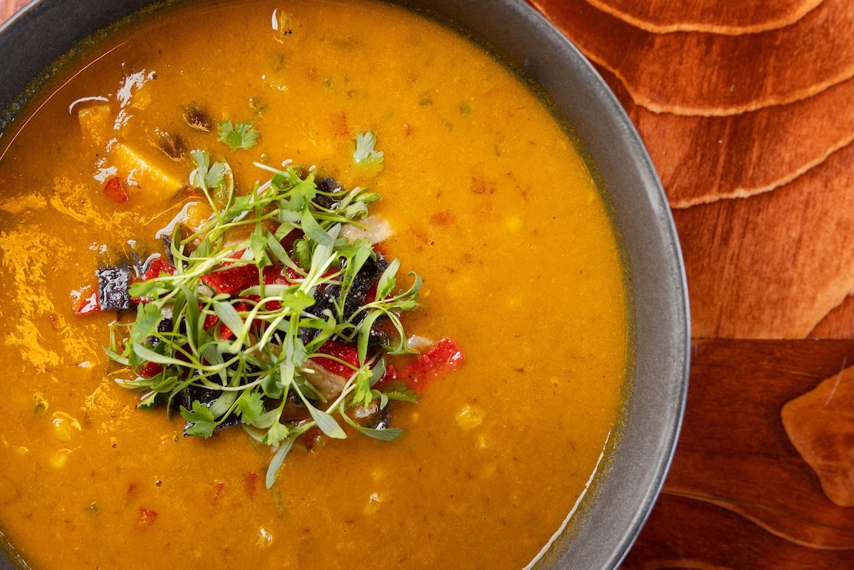 A bowl of orange soup with herb garnish on a wooden table.