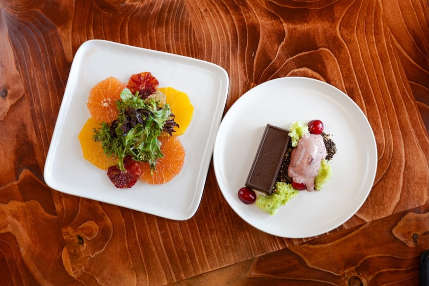 Two white plates with a citrus salad and a chocolate dessert on a wooden table.