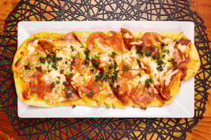 Rectangular flatbread pizza with pepperoni, cheese, and herbs on a white plate.