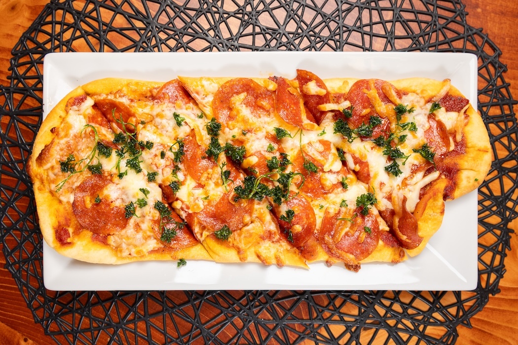Rectangular flatbread pizza with pepperoni, cheese, and herbs on a white plate.
