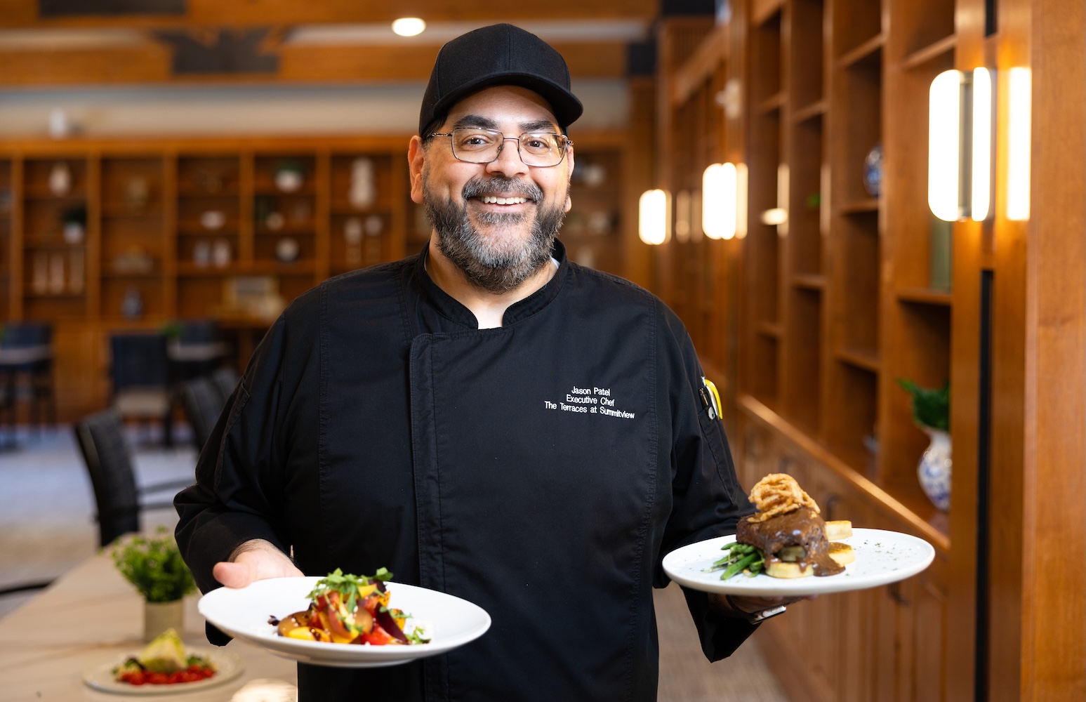 Chef in a black uniform holding two plates of food in the bistro