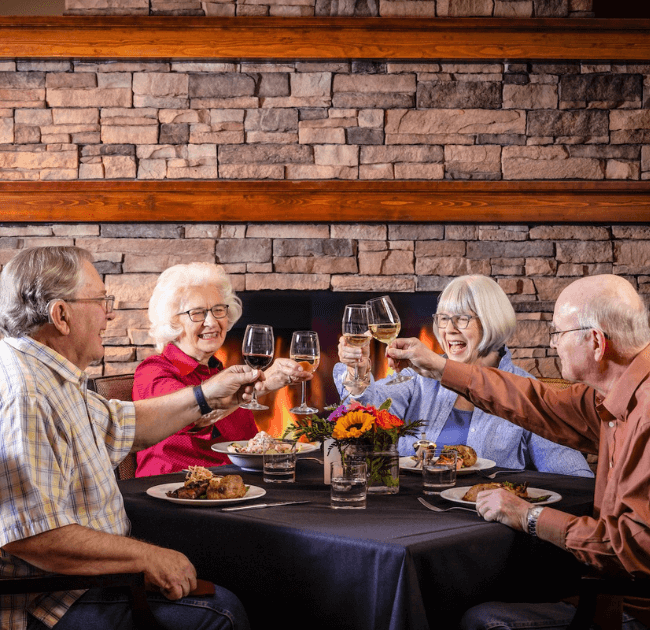 Four seniors toasting with wine glasses at dinner in The Terraces of Boise dining room