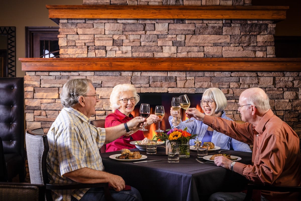 Four seniors toasting with wine glasses at dinner in The Terraces of Boise dining room