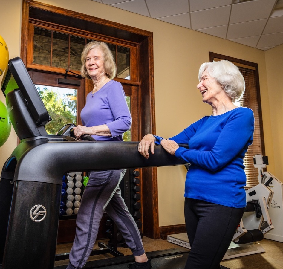 Two women in an exercise room while one is on the treadmill