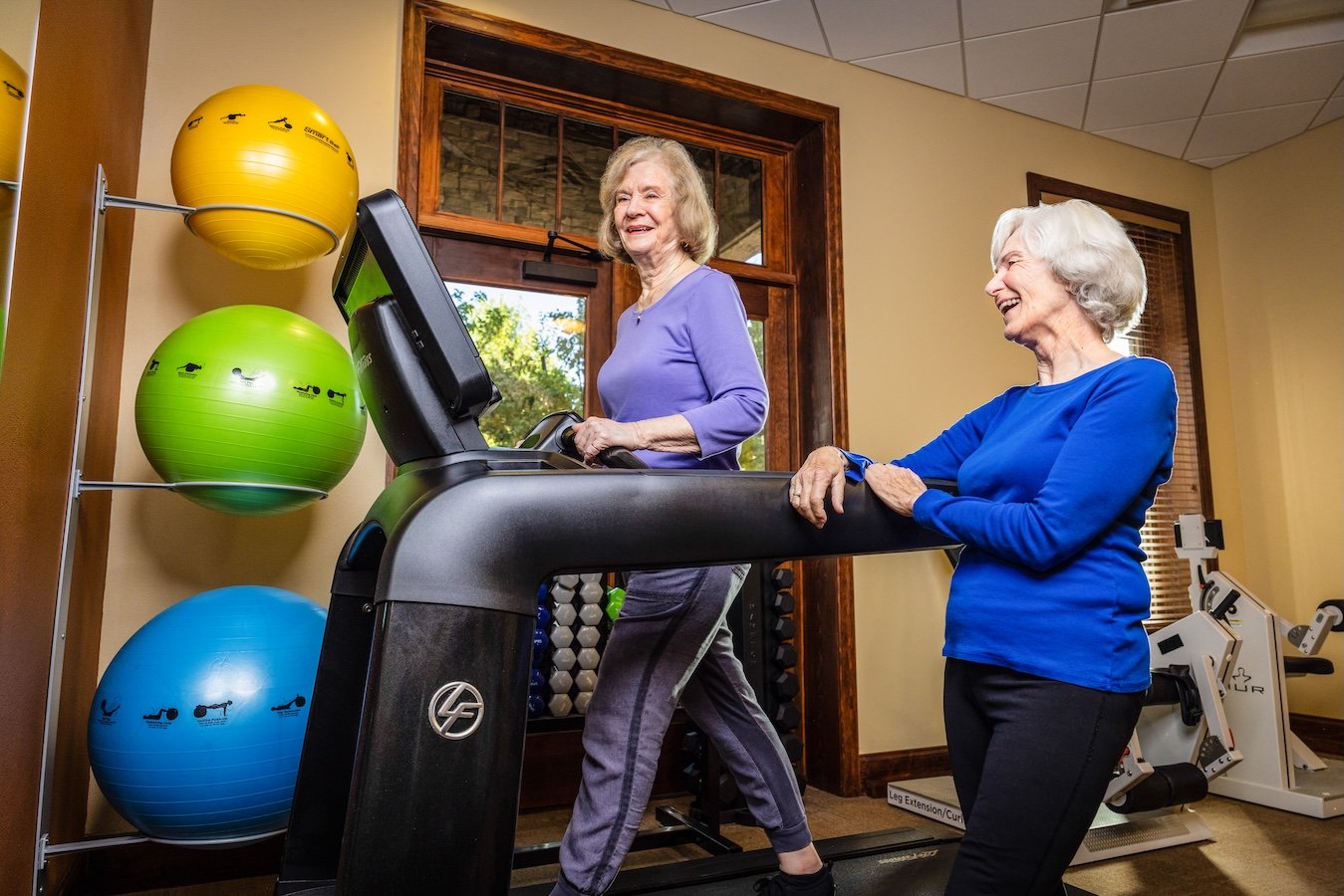 Two women in an exercise room while one is on the treadmill