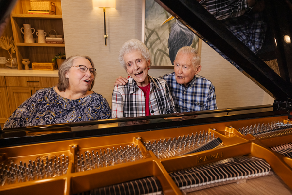 Two senior women and a senior man playing the piano and singing