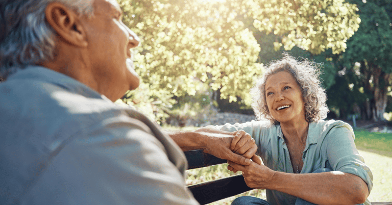 senior couple holding hands on a bench smiling at each other