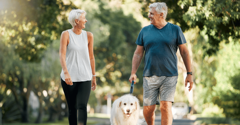 man and woman smiling and walking dog outside
