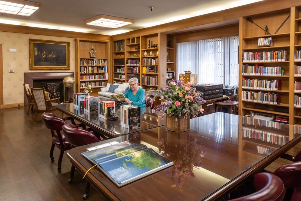 Senior woman reading a book at a table in the Westminster Gardens library