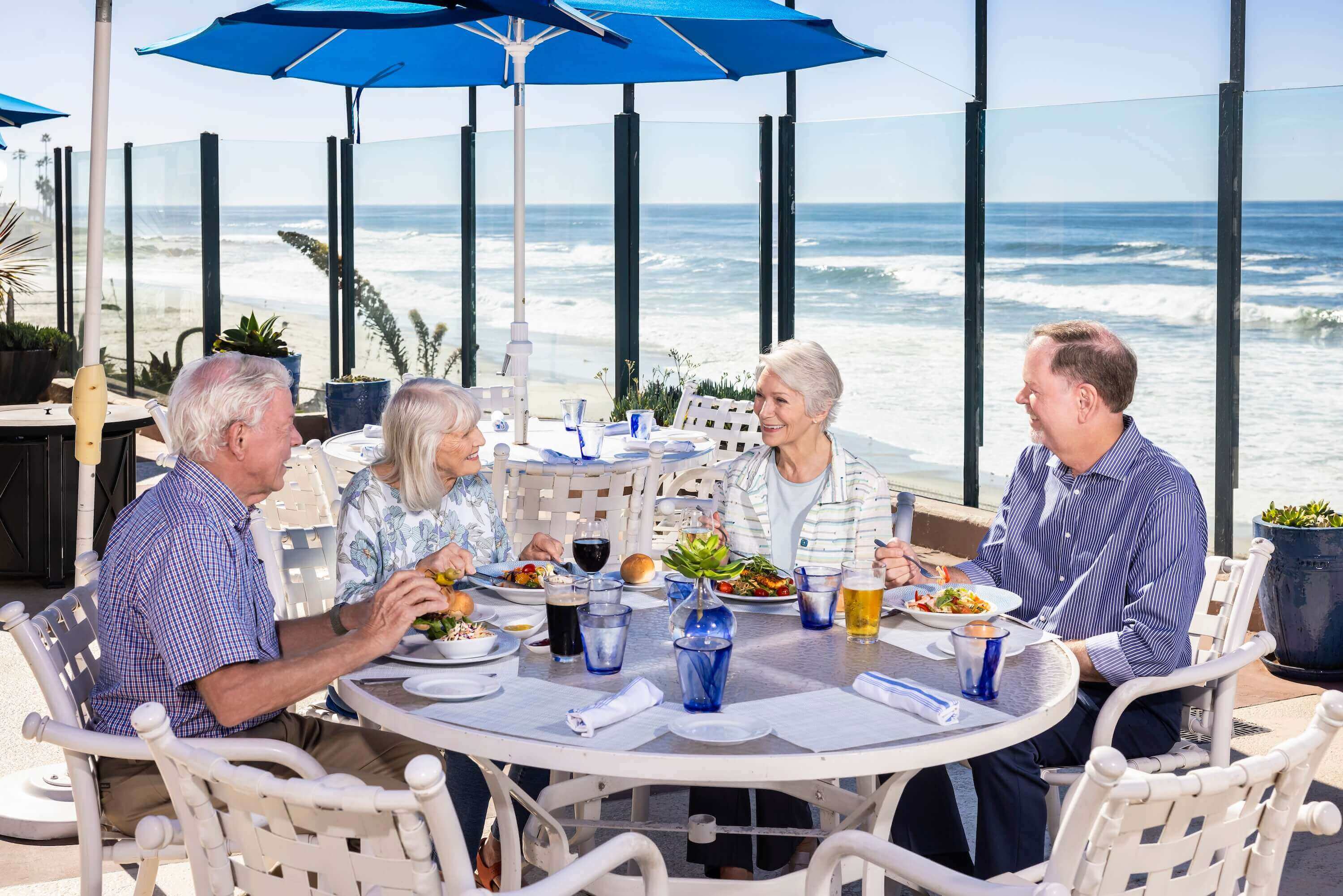 Older adults dining together at an outdoor oceanfront restaurant.