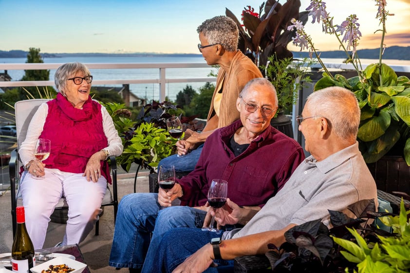 Residents socializing with drinks on an outdoor terrace overlooking the water at Judson Park, a HumanGood community.
