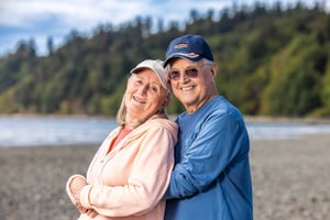 Residents standing together on a beach with trees and water in the background near Judson Park, a HumanGood community.