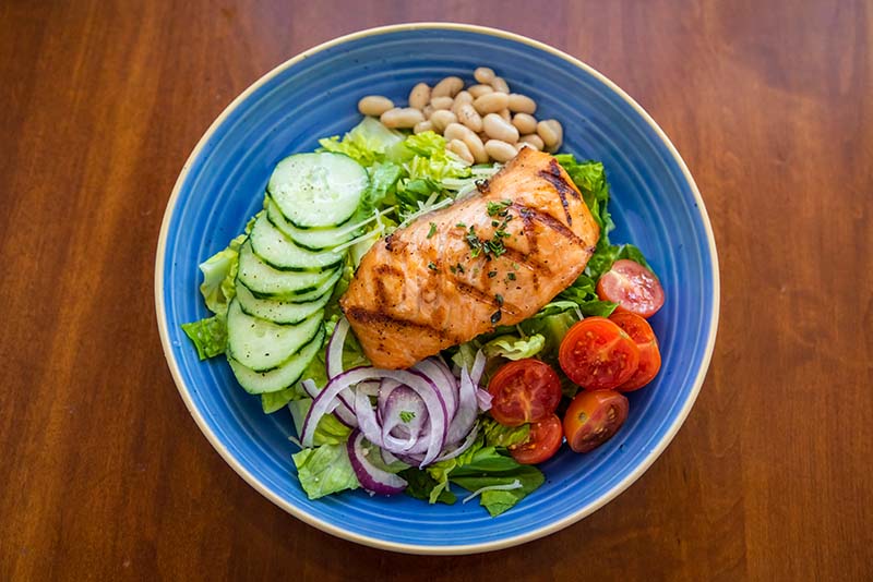 Healthy salmon salad with lettuce, tomato, beans, onion and cucumber