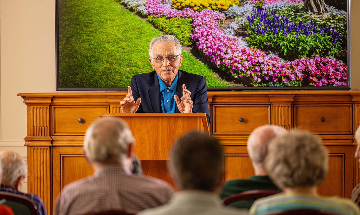 senior man at a podium performing a lecture to a crowd of senior residents