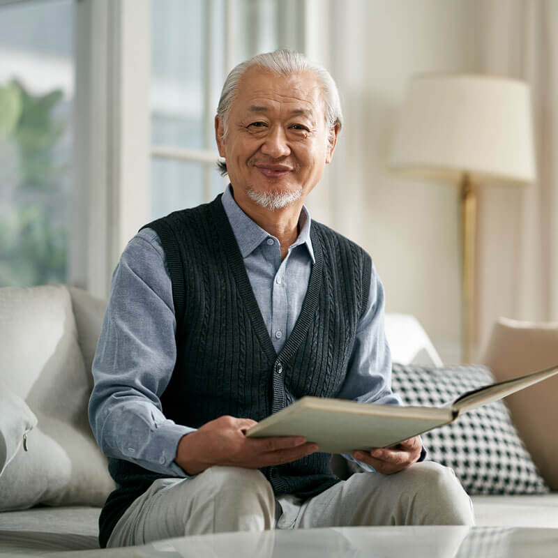 Senior man sitting on couch holding a book and smiling