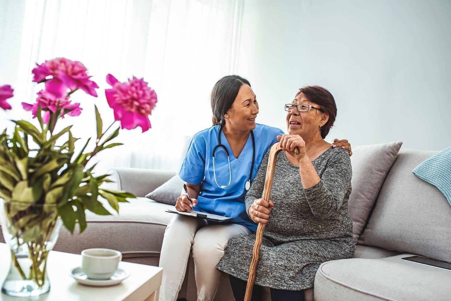 Smiling female medical professional and senior woman with a cane sitting on a couch