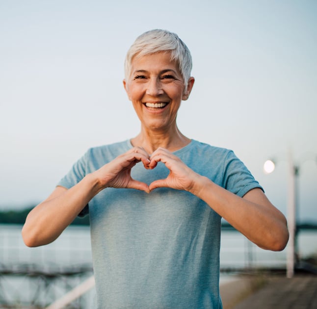 Senior woman standing on dock holding hands in a heart shape