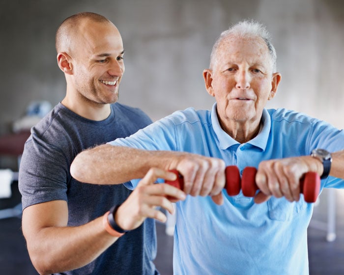 Male physical therapist helping senior man lift weights
