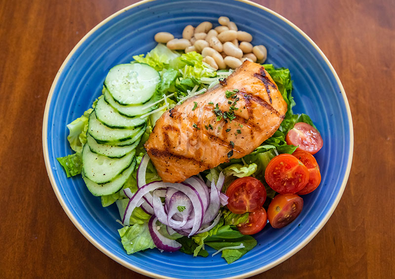 Salmon filet on a bed of lettuce, cucumber, onion, tomato, and beans