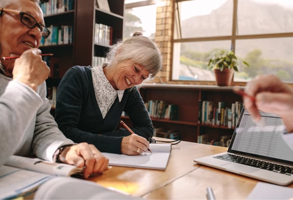 Senior woman and man at a table in the library writing in notebooks