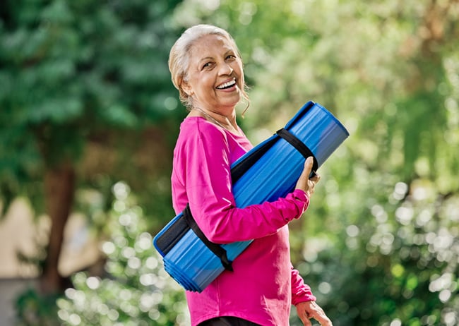 senior woman holding yoga mat outside and smiling