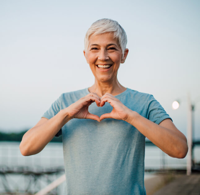 Senior woman standing on dock holding hands in a heart shape