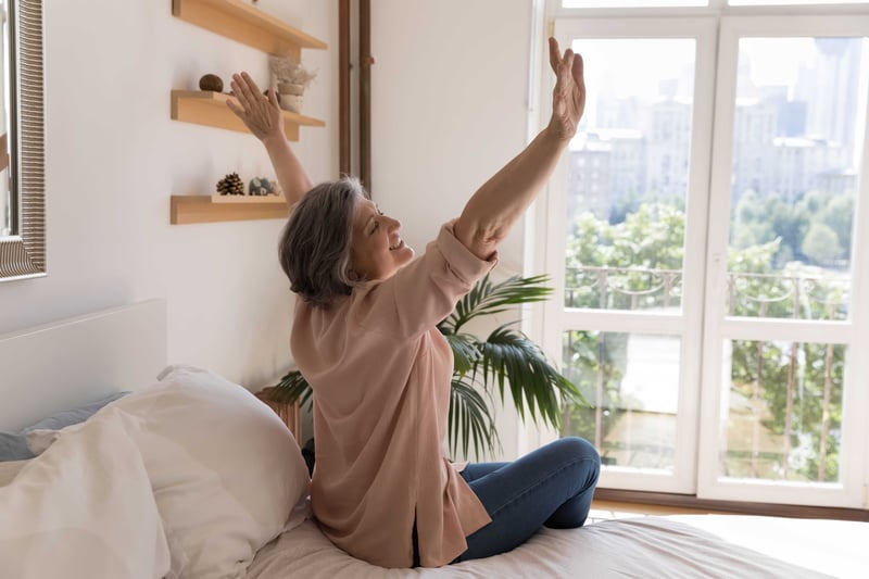 A woman embracing the sun that shines through her bedroom windows.