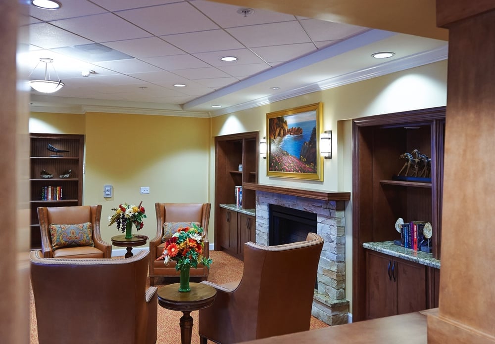 Side view of a common living room area with a chimney and books at senior living community The Terraces at Los Altos