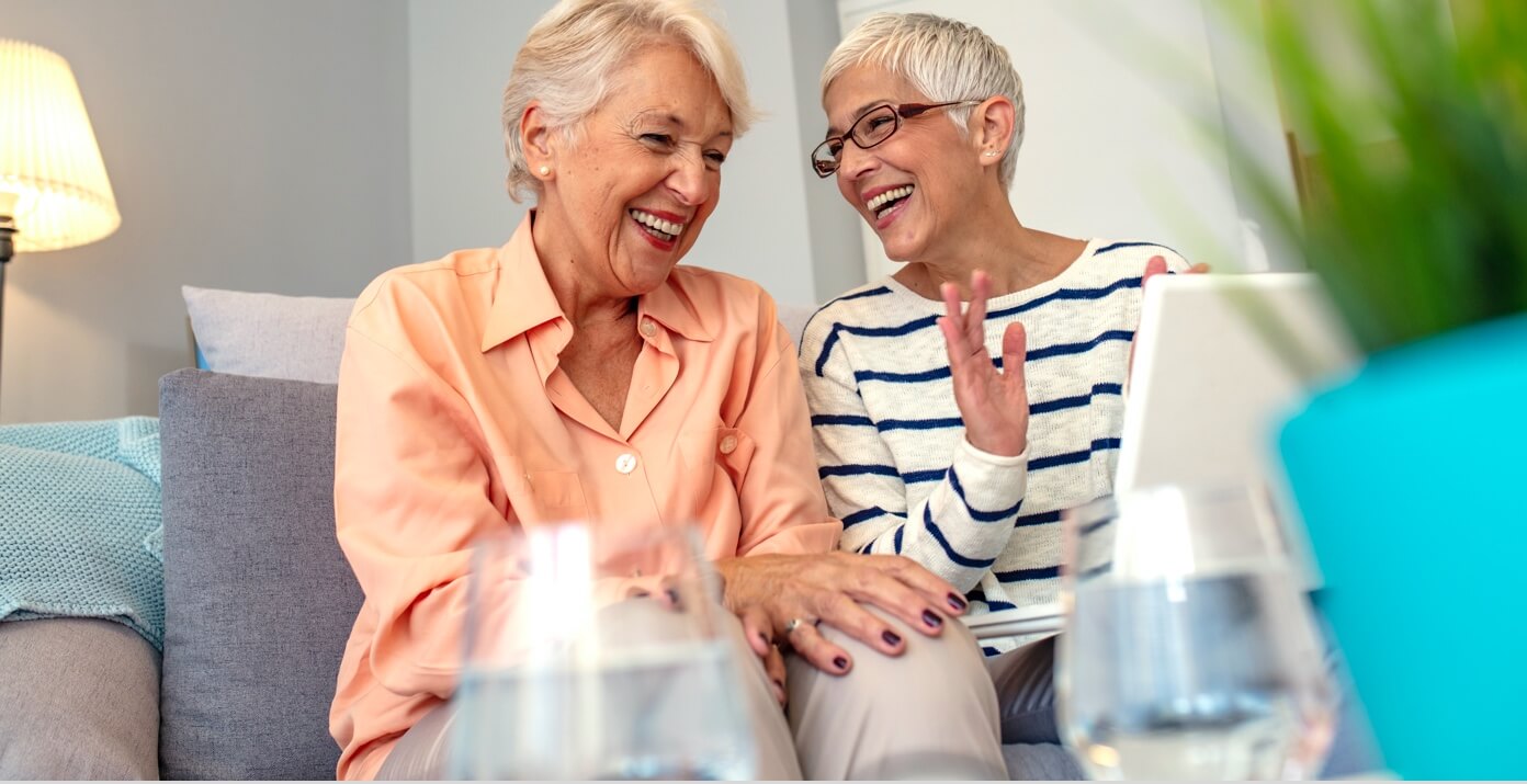 Two senior women sitting on couch laughing