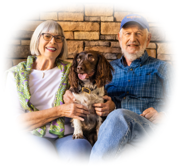 Tom and Mary sitting with their brown and white dog on a bench in front of a brick wall