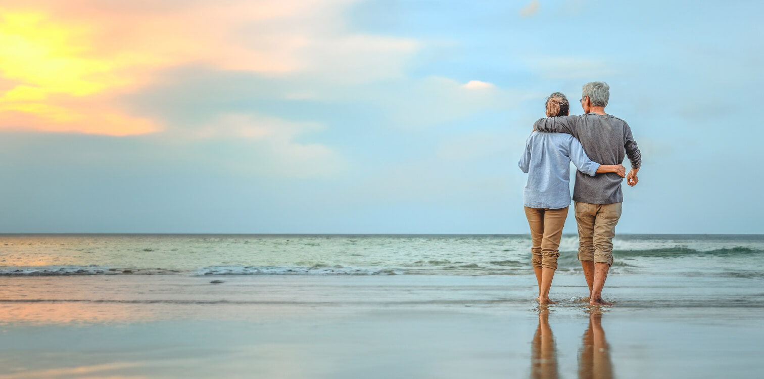 Senior couple with their arms around each other walking on the beach