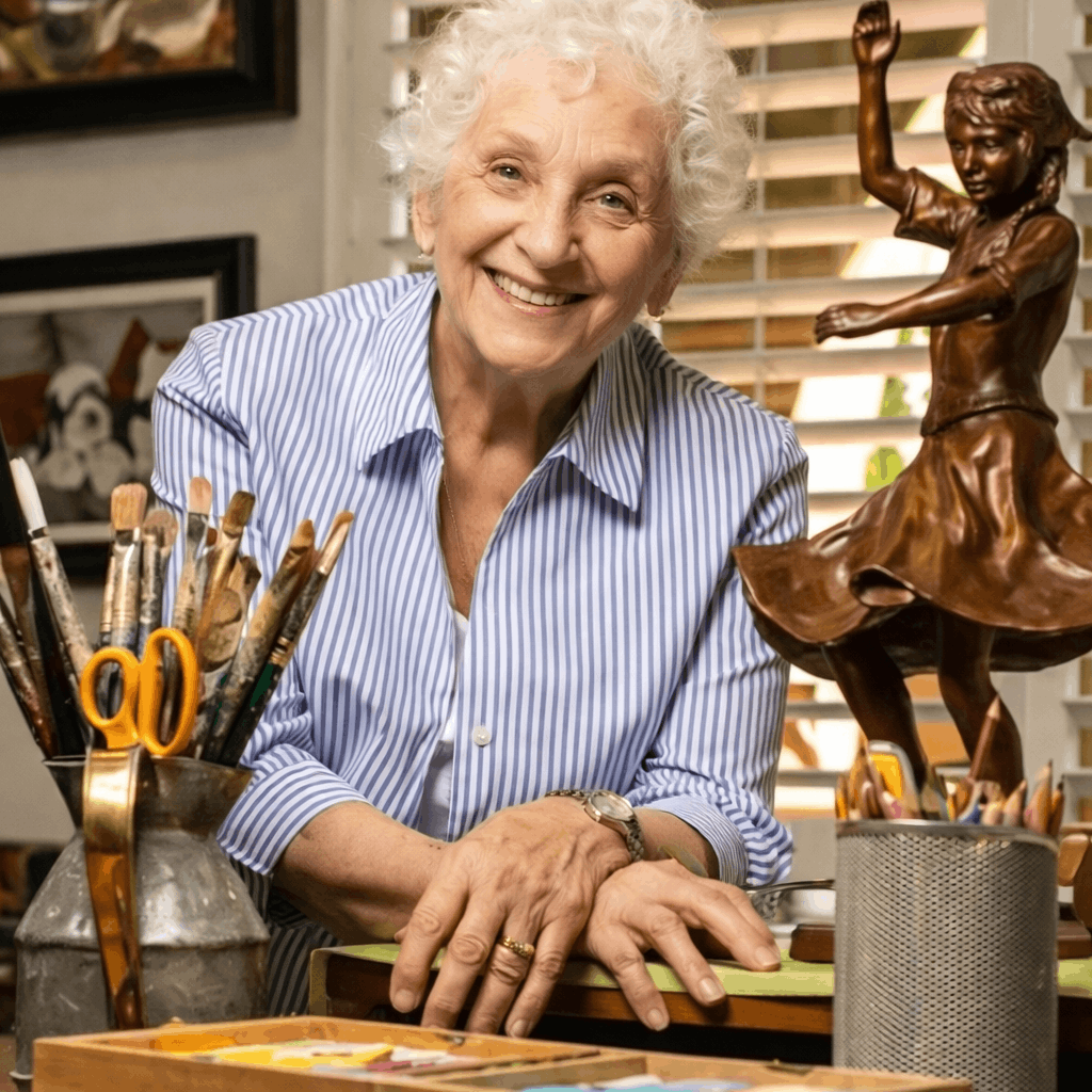 Smiling resident at an art desk with paintbrushes and a sculpture in a creative studio.