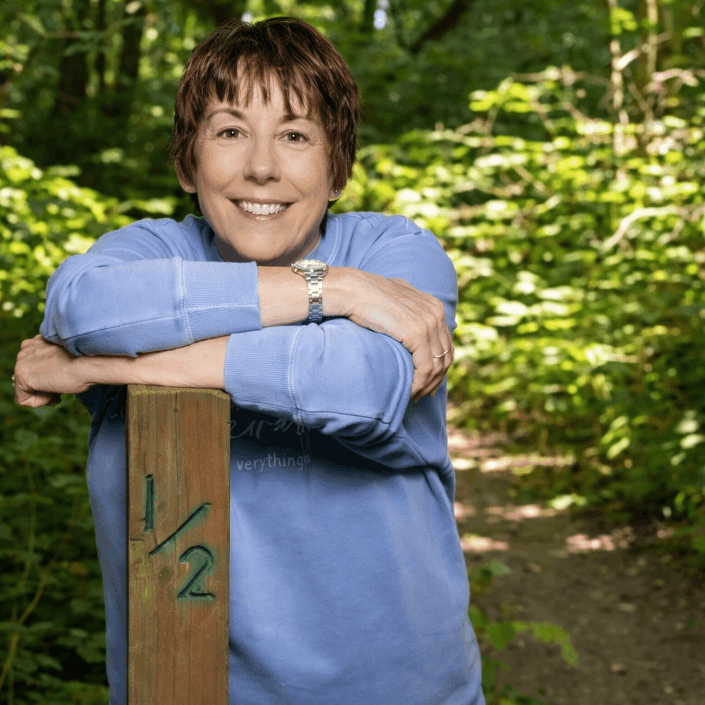Smiling resident named Sara wearing red glasses and a red jacket, seated indoors.