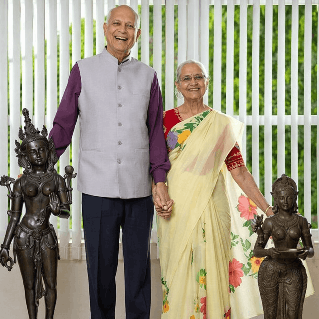 Smiling couple holding hands indoors, standing beside decorative sculptures.