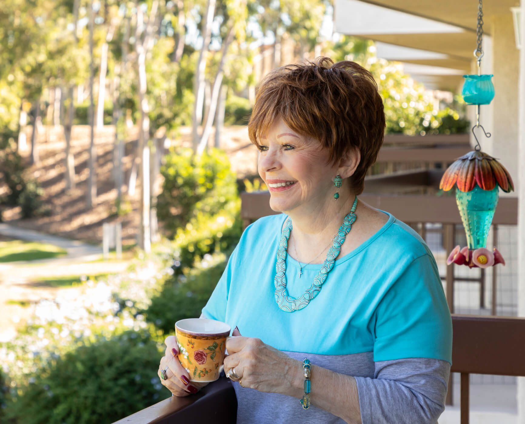 Senior woman standing on a balcony holding a mug and smiling
