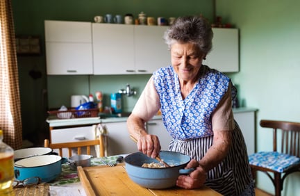 Senior woman mixing ingredients with a wooden spoon in a blue bowl in kitchen