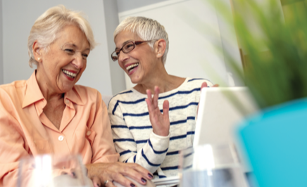 Two senior women sitting next to each other while laughing