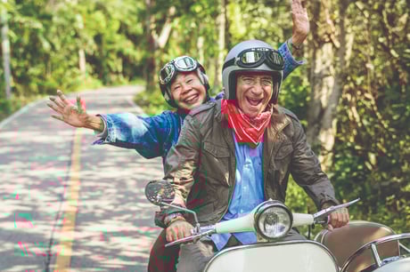 A couple laughs while riding an electric scooter down the road.