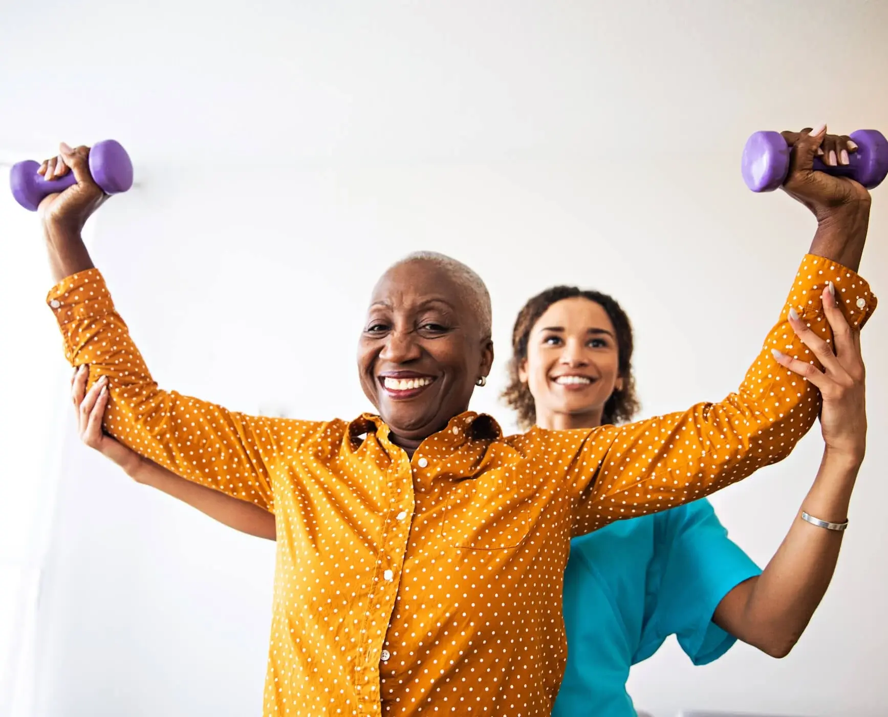 Smiling woman lifts purple dumbbells while a trainer supports her arms.