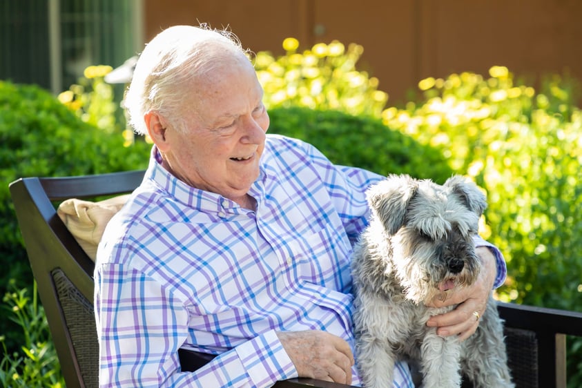 senior sitting outdoors with a small dog on his lap