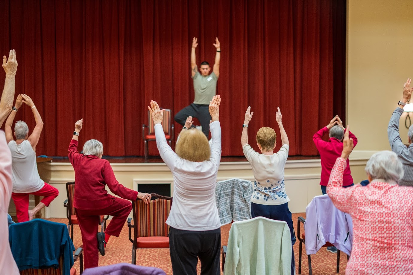 Seniors taking a chair fitness class with an instructor on the stage