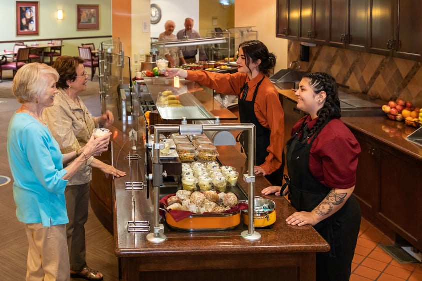 Two senior women standing at a pastry counter ordering from two young female employees