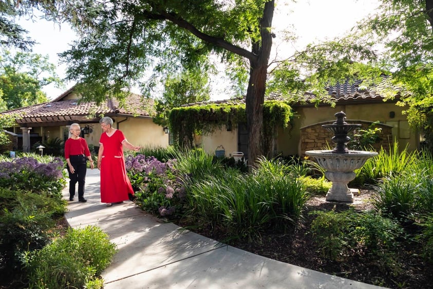 senior women wearing red while walking a paved garden path