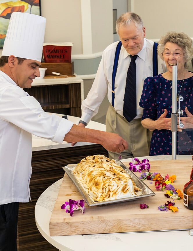 Senior couple at a carving station watching a chef carve meat in a dining room at Rosewood