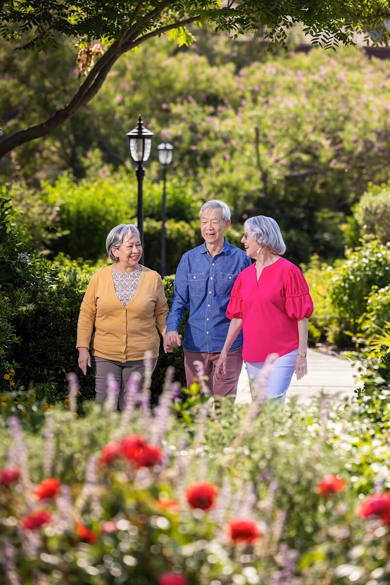 Two senior women and a senior man walking on a path through a HumanGood Life Plan Community