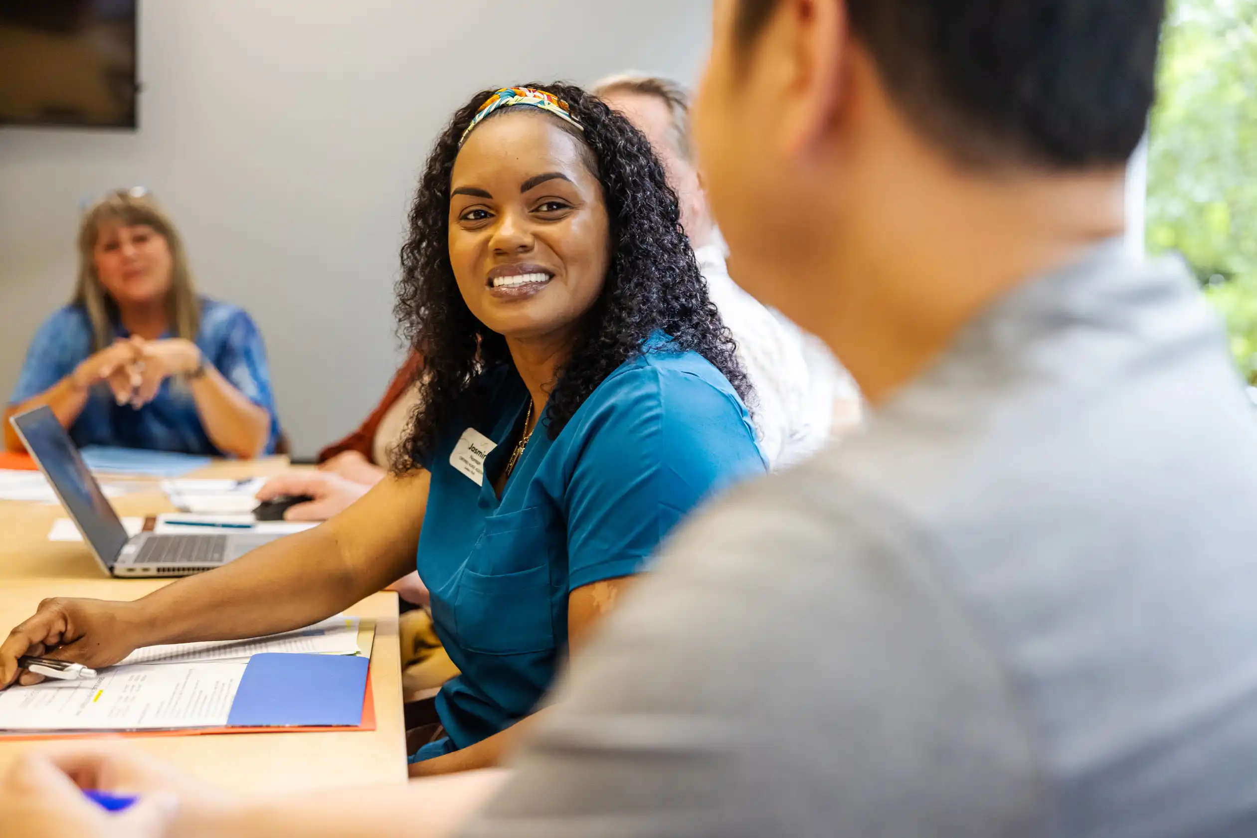 woman wearing scrubs smiling at colleague in a meeting
