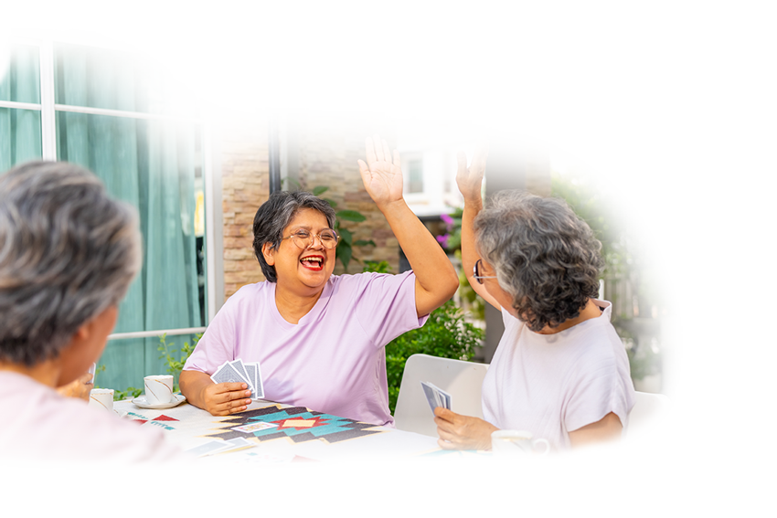 senior women playing cards, two women smiling and giving each other high fives